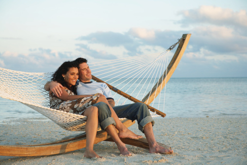 Couple smiling in hammock on beach, side view